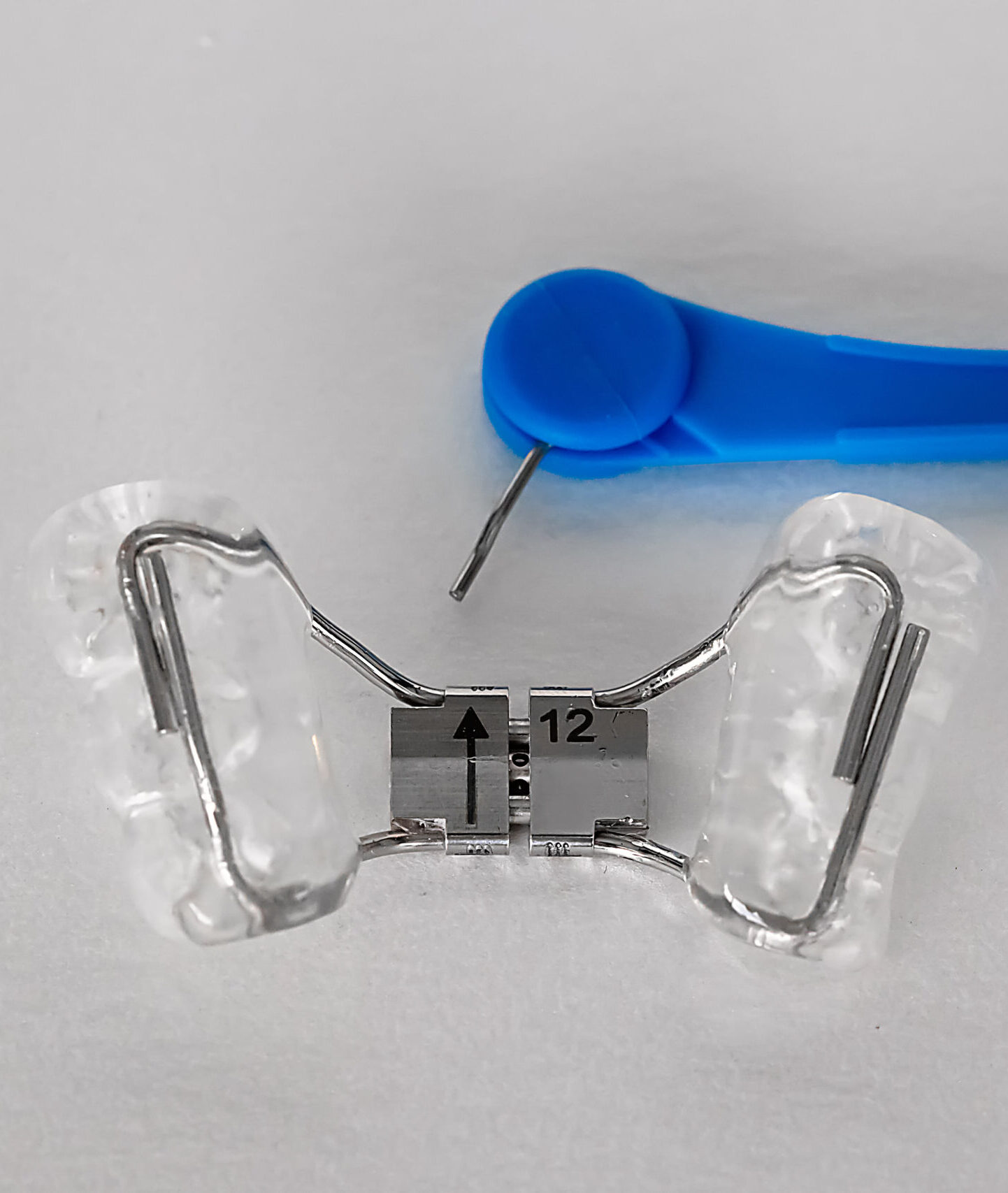 Orthodontic palatal expander and blue adjustment key on white background. Removable dental appliance used to widen the upper jaw in orthodontic treatment.