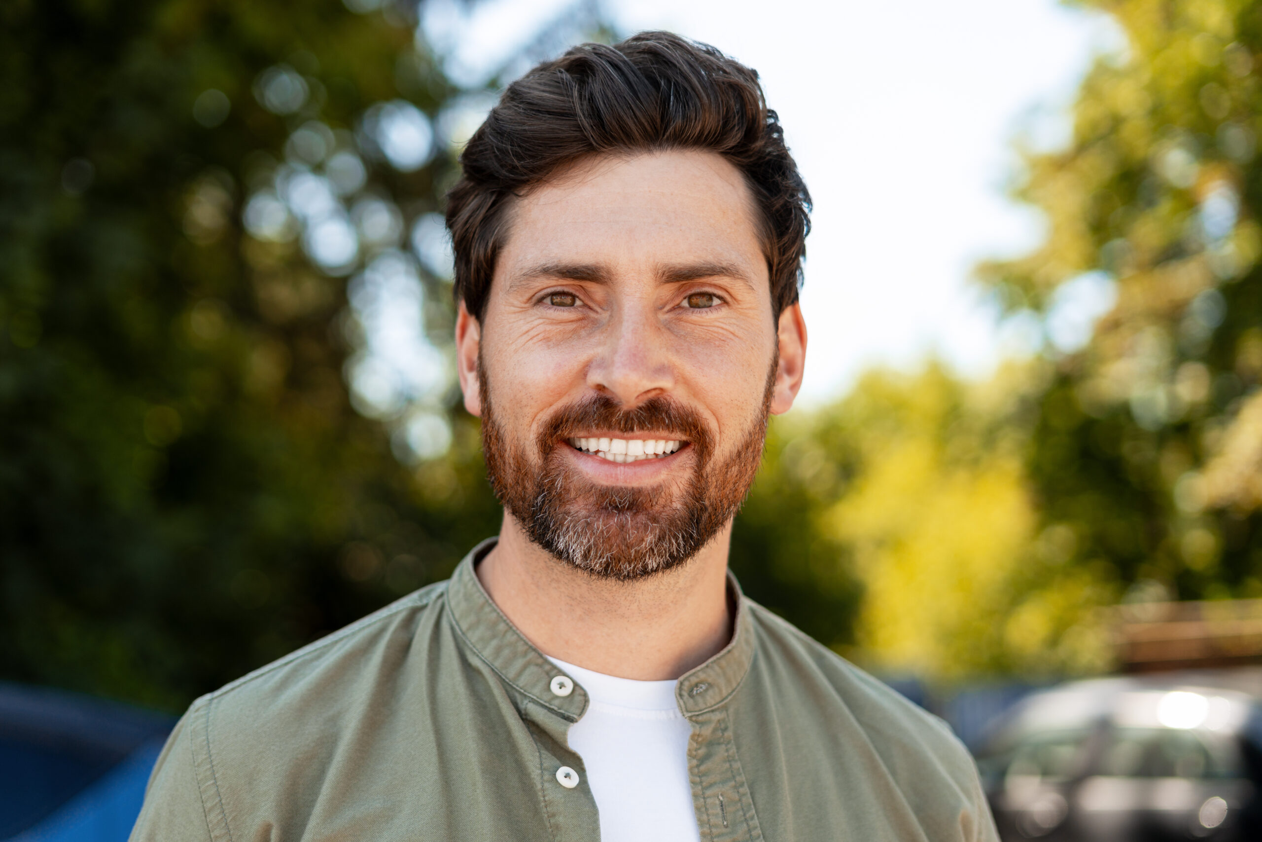 Confident businessman smiling while standing outdoors on a sunny summer day, exuding professionalism and a sense of achievement