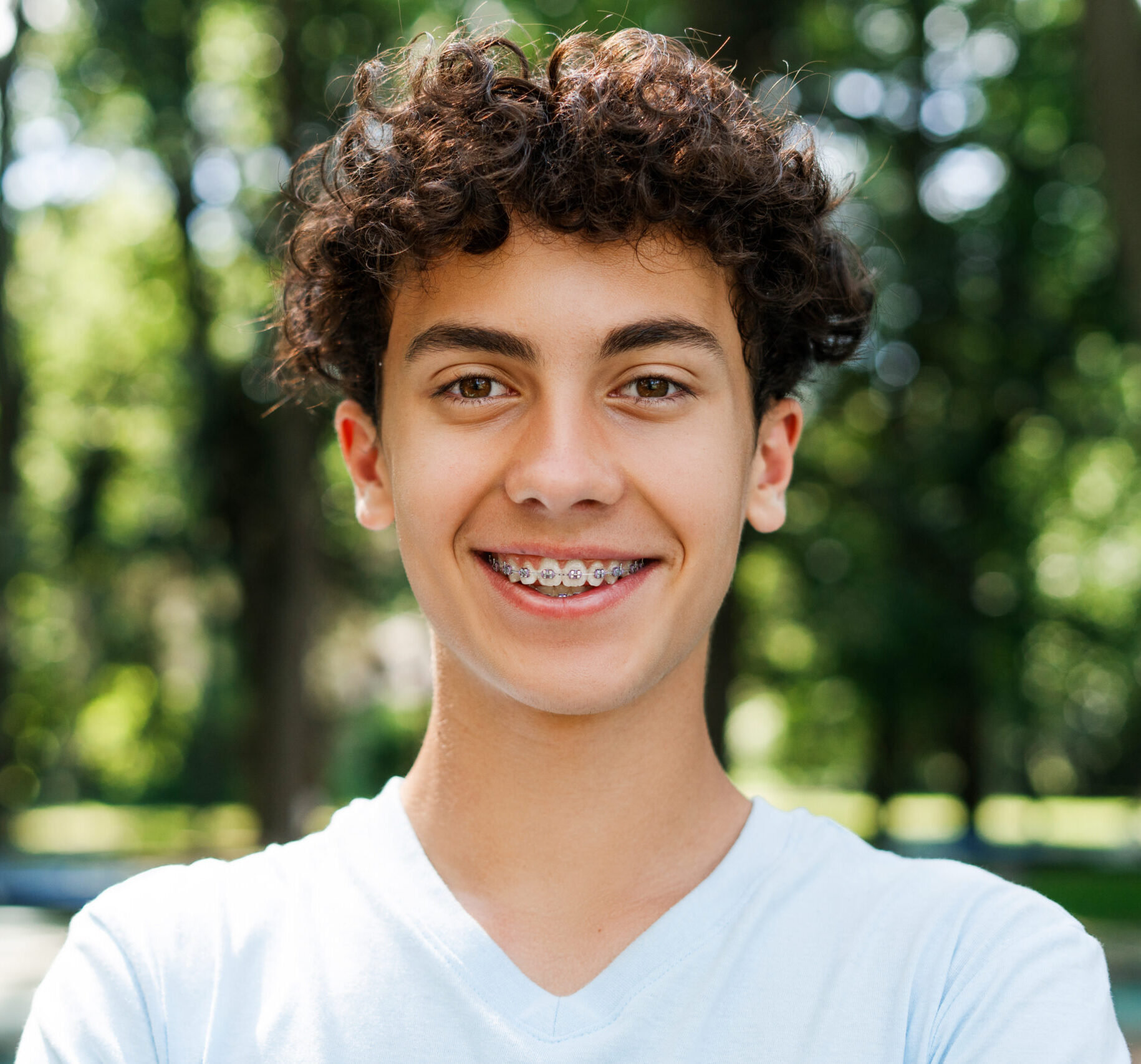 Positive teenager boy with braces looking at camera in the park